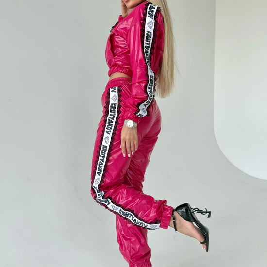 Fuchsia shiny women’s tracksuit set with cropped zip jacket, branded side stripes, and matching jogger pants