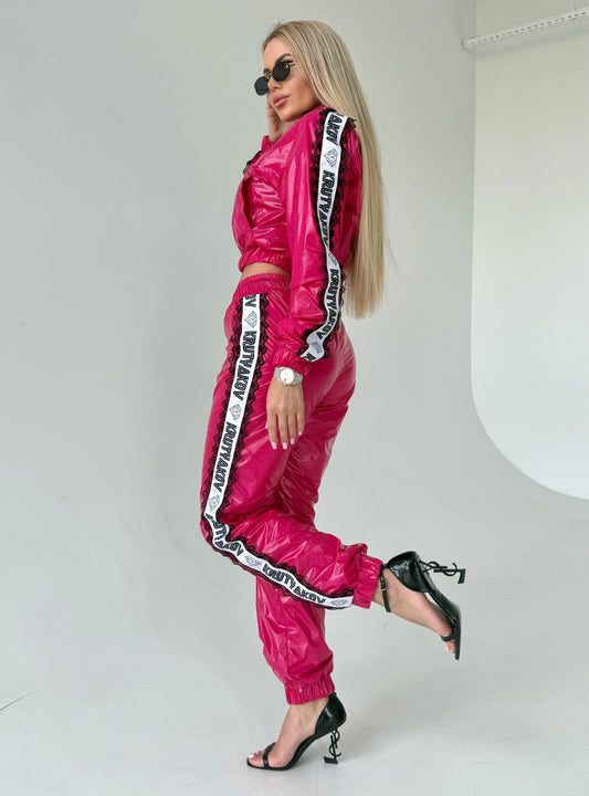 Fuchsia shiny women’s tracksuit set with cropped zip jacket, branded side stripes, and matching jogger pants