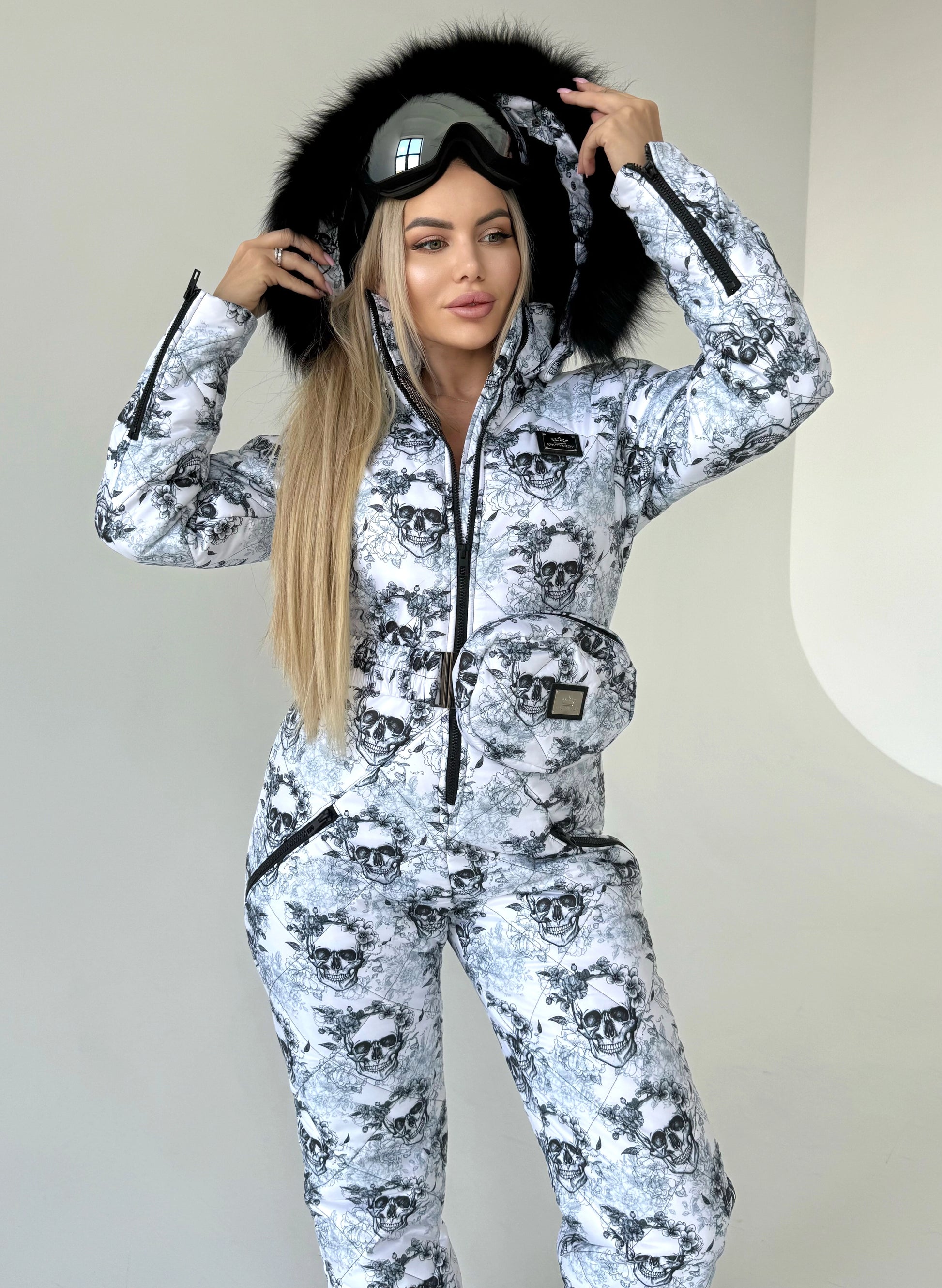 Full-body view of women’s black white skull ski suit with belt bag, hood, and winter-ready one-piece design