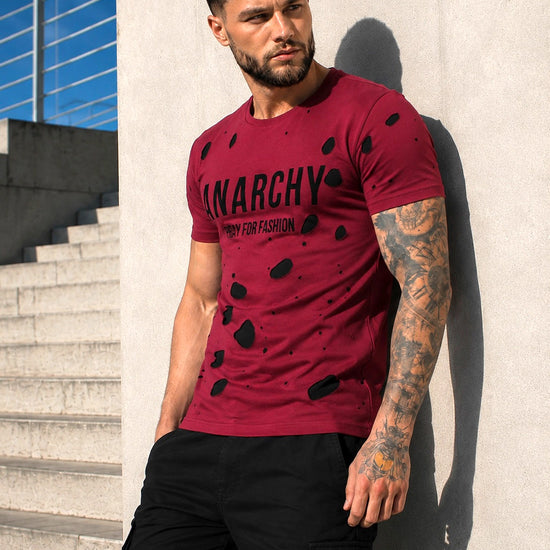 Male model wearing a burgundy ANARCHY graphic T-shirt with black pants in an urban streetwear look