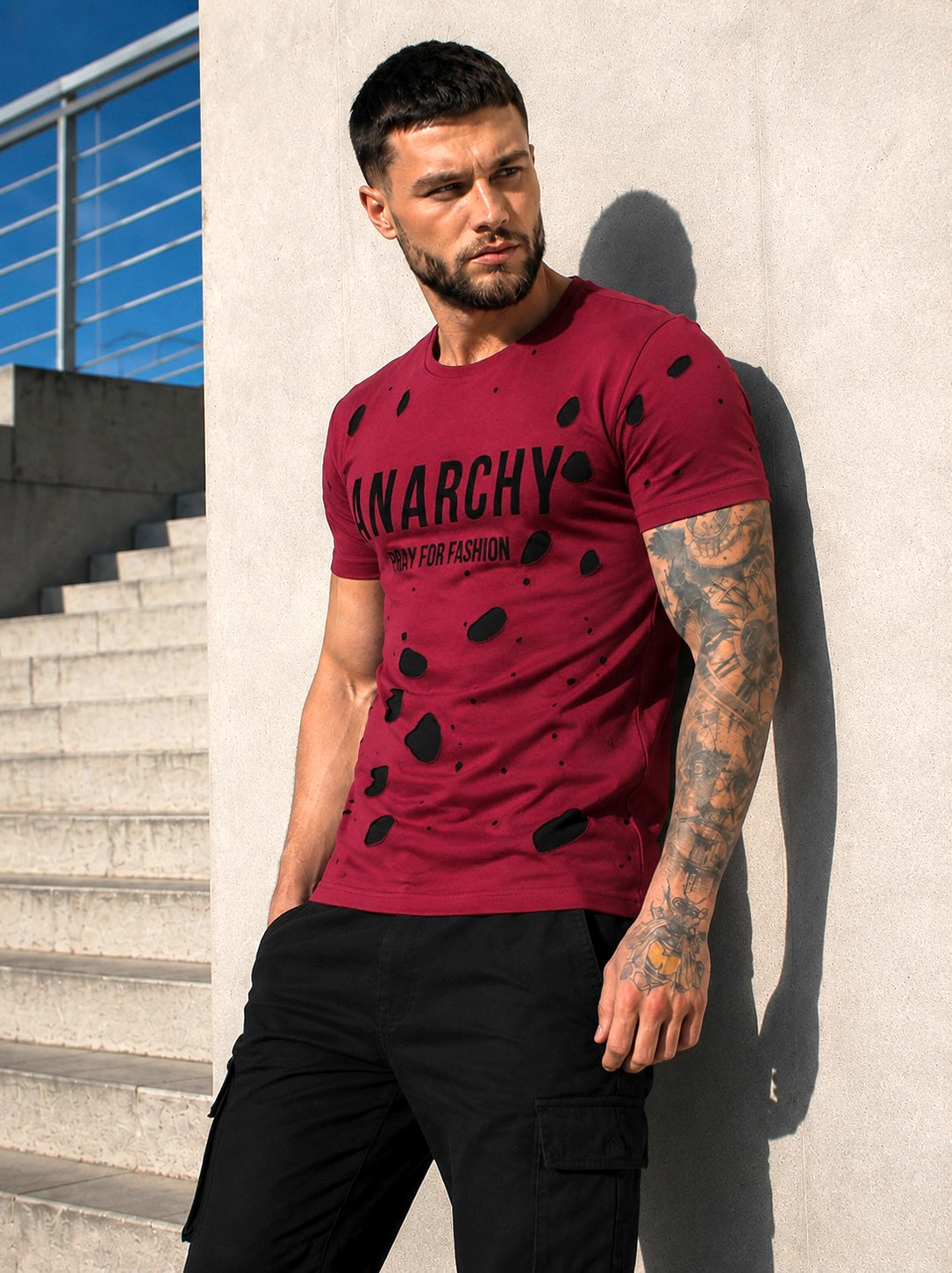 Male model wearing a burgundy ANARCHY graphic T-shirt with black pants in an urban streetwear look