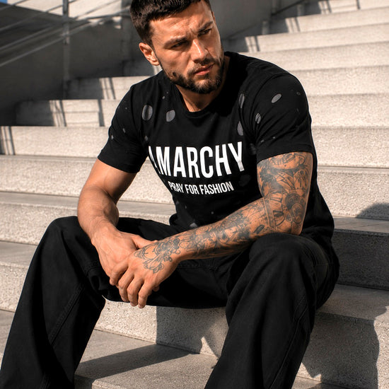 Male model sitting on steps wearing a black ANARCHY graphic T-shirt and black pants