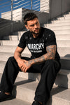 Male model sitting on steps wearing a black ANARCHY graphic T-shirt and black pants