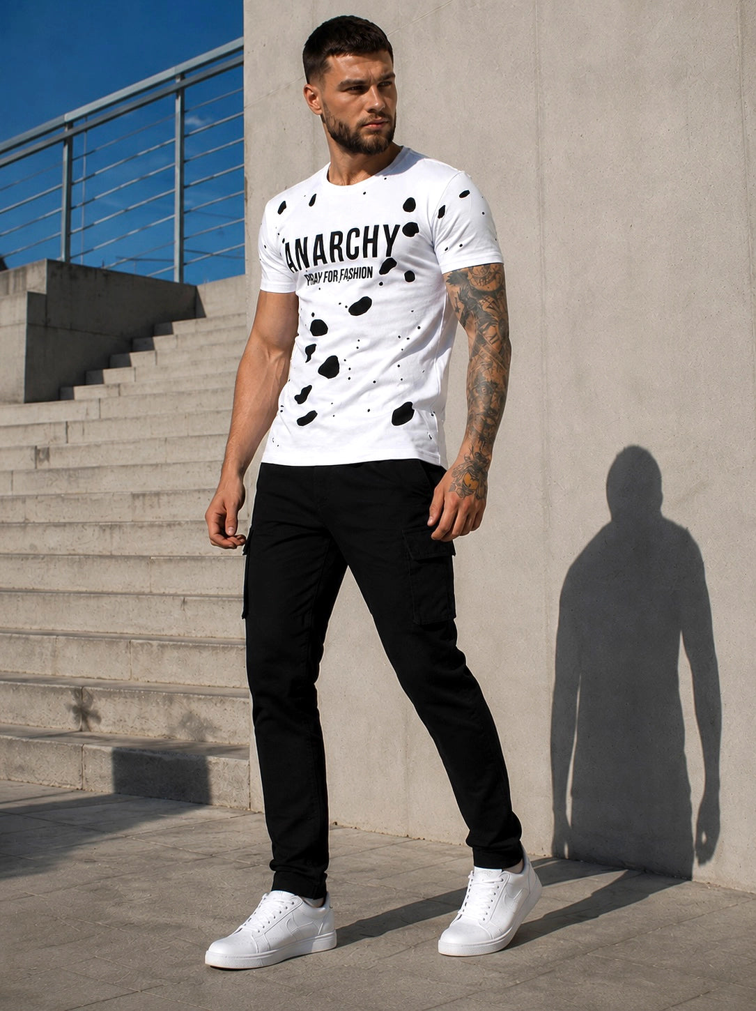 Male model wearing a white ANARCHY graphic T-shirt with black pants and white sneakers